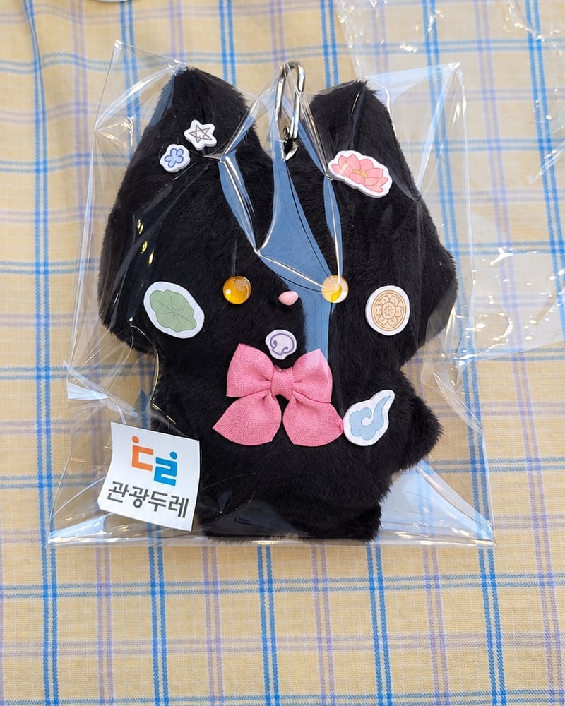 분홍 리본과 참으로 꾸민 검은 고양이 인형이 포장된 모습